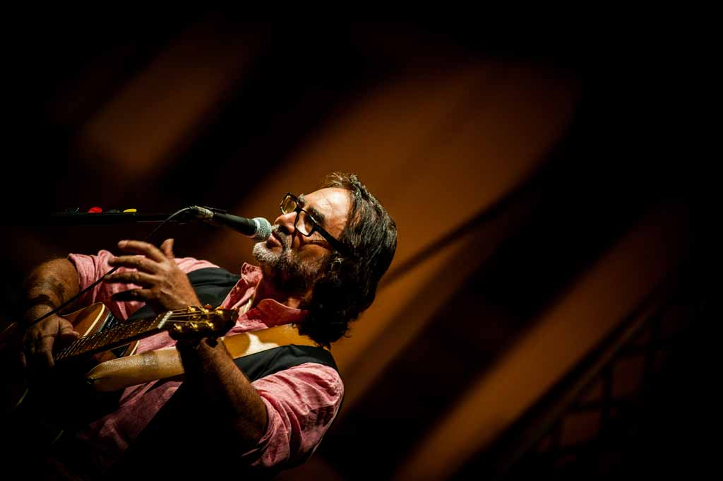 Carlo Muratori canta al microfono con la chitarra, durante un concerto