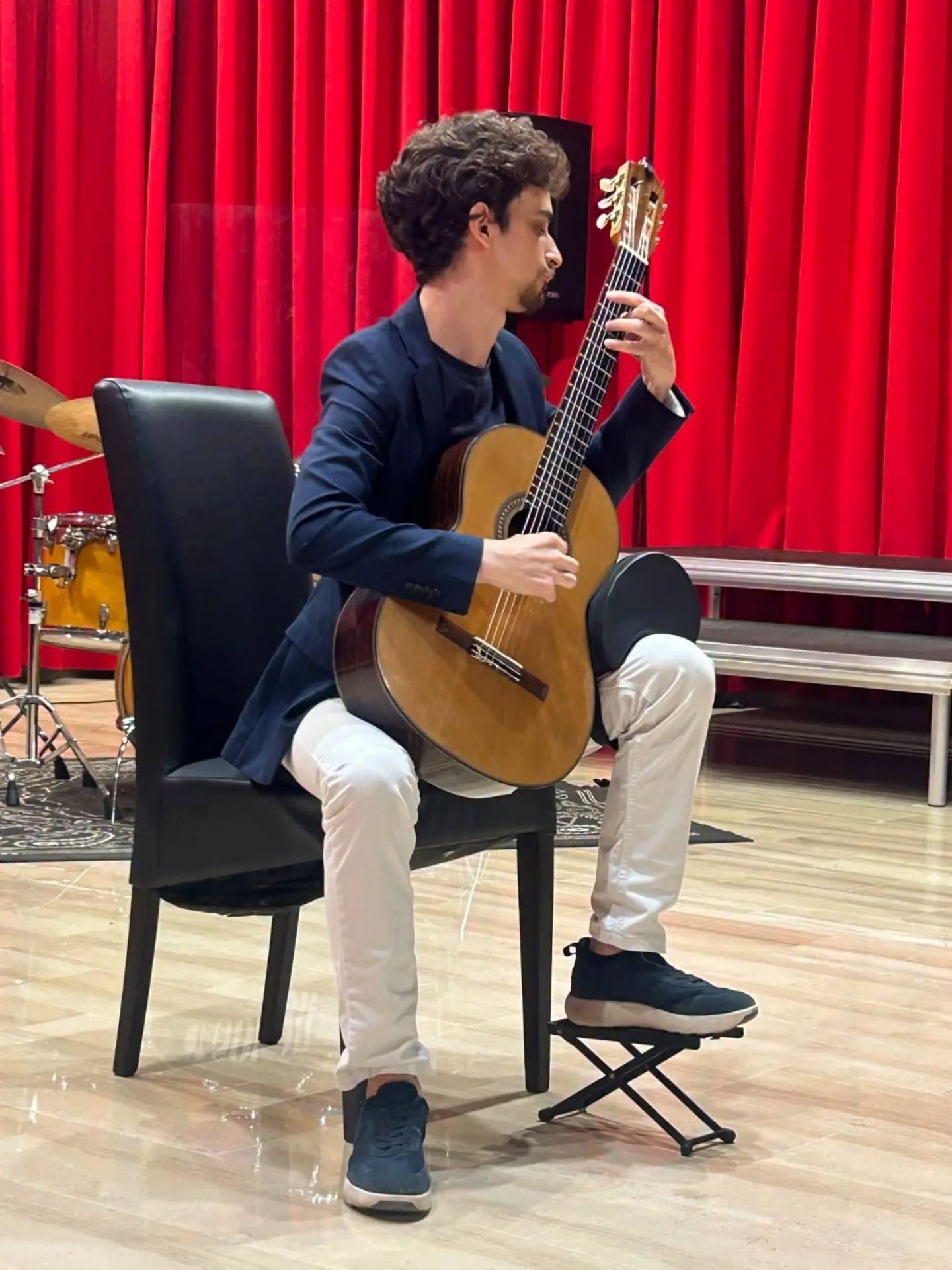Ferdinando Fallica suona la chitarra classica davanti a un sipario rosso