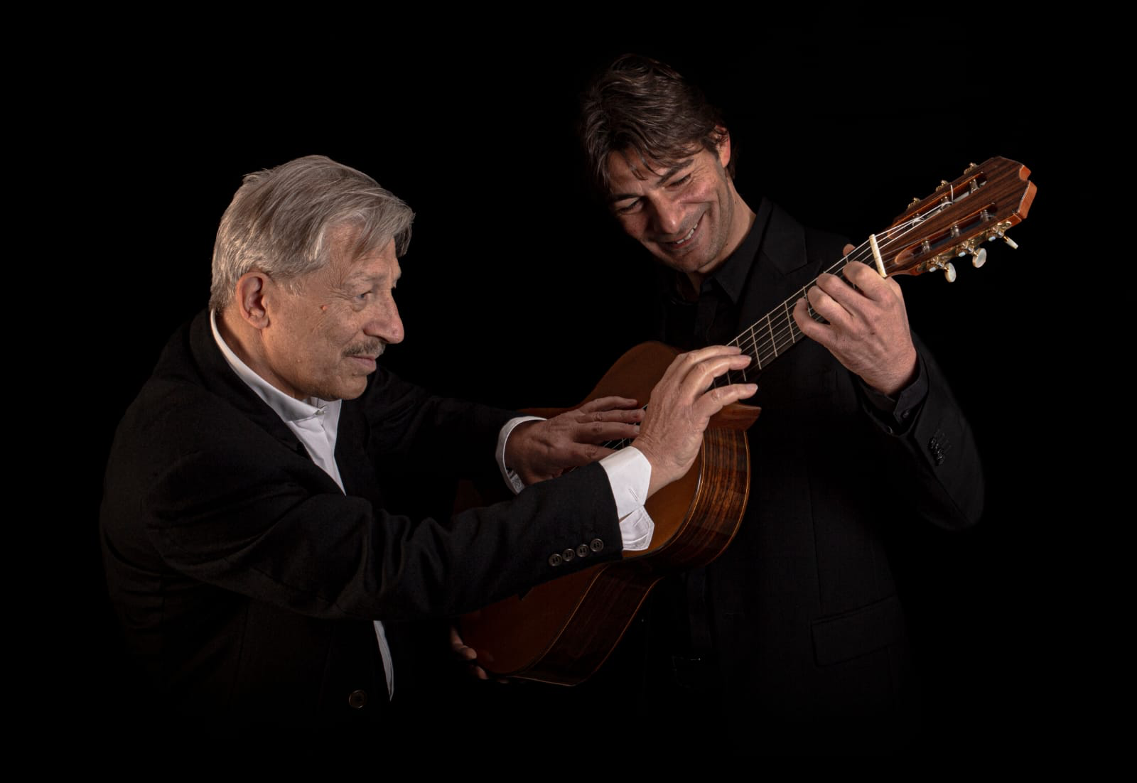 Nello e Simone Alessi suonano insieme una chitarra su sfondo nero